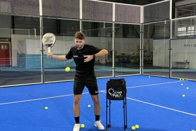 Raquette de padel, entraînement sportif dans un centre indoor, moniteur de padel, sol en tapis bleu, balles de padel dispersées, enseigne Next Point, coach de padel, équipements de sport, salle de sport spécialisée, entraînement de tennis de plage, centre de sport et loisirs, activité physique en intérieur.