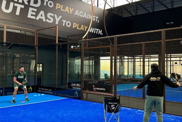 Les joueurs de padel s'entraînent dans une salle intérieure moderne avec un sol bleu et un filet sécurisé, ambiance dynamique pour la pratique du padel à São João.
